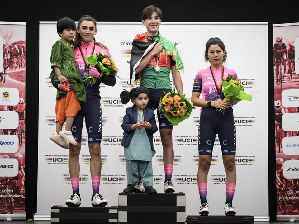 Drei Radrennfahrer und zwei Kinder auf dem Podium, die Blumensträusse halten.