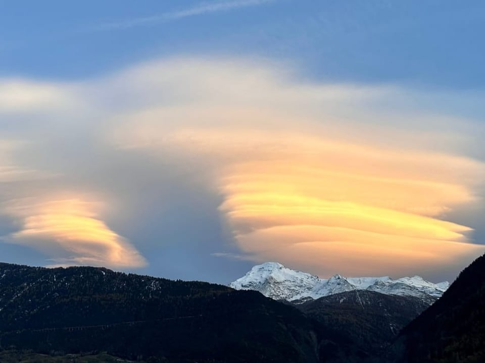 Berge im Vordergrund mit wellenförmigen Wolken bei Sonnenuntergang.