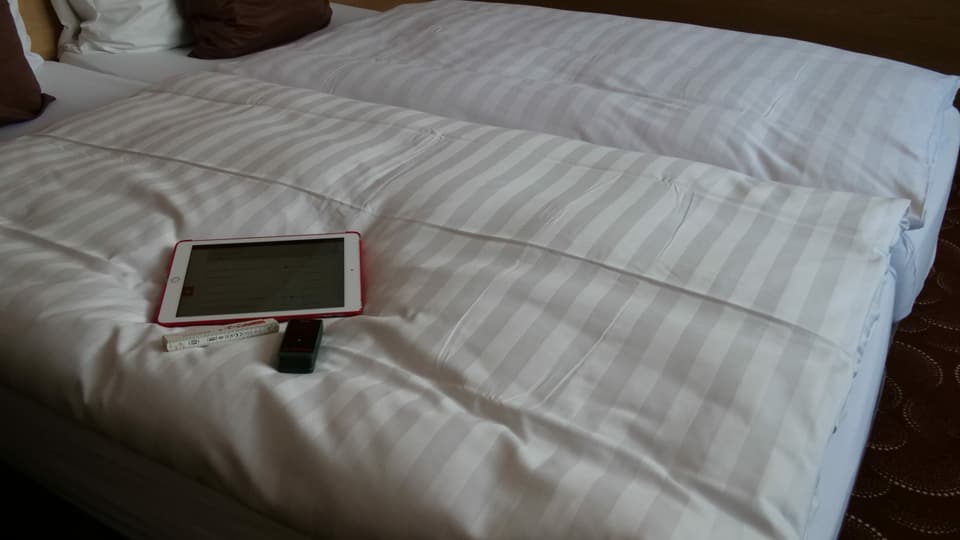Tablet, Doppelmeter und Messgerät liegen auf dem Hotelbett.