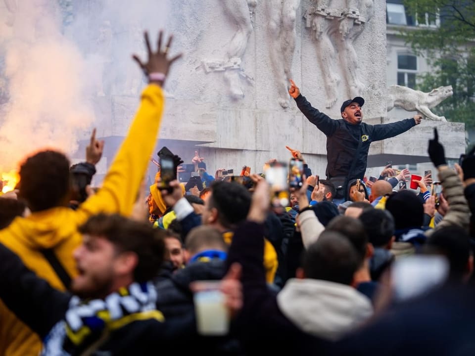 Menschenmenge bei einer Feier mit jubelnden Fans vor einem Denkmal.