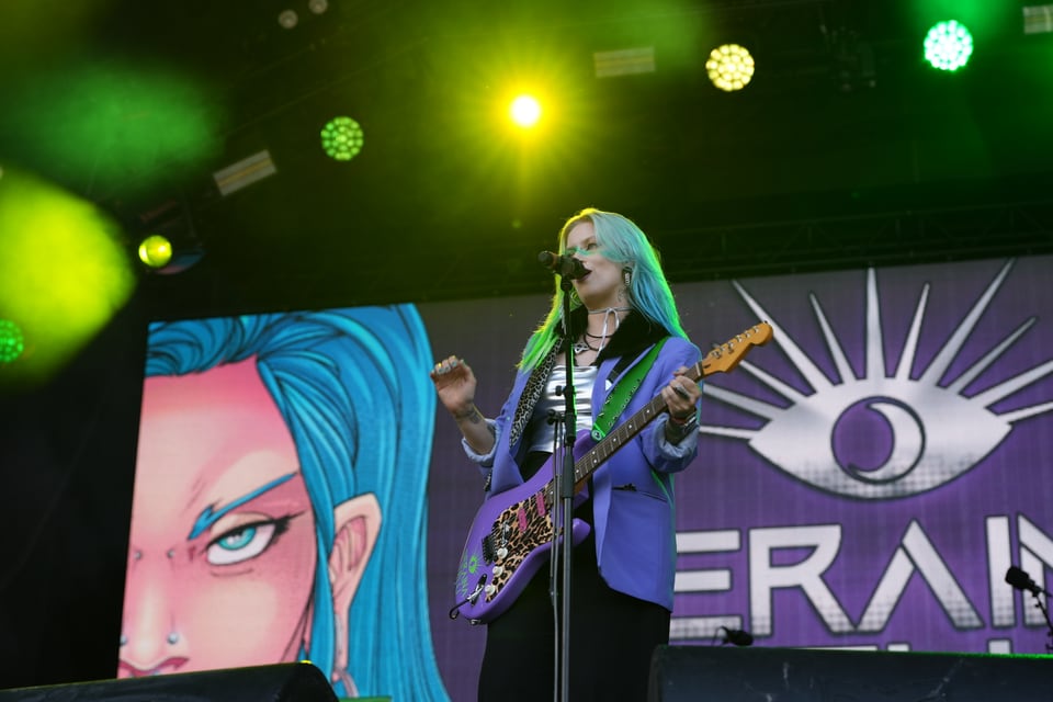 Frau mit blauen Haaren und Gitarre auf der Bühne am Open Air Lumnezia 2024.