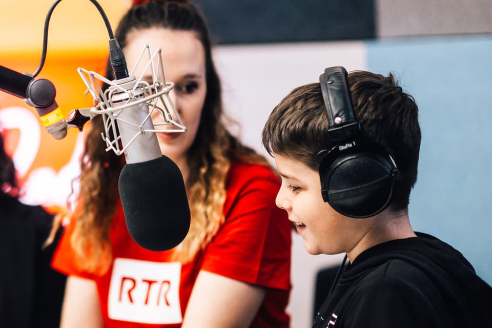 Frau und Junge mit Kopfhörern im Radiostudio am Mikrofon.