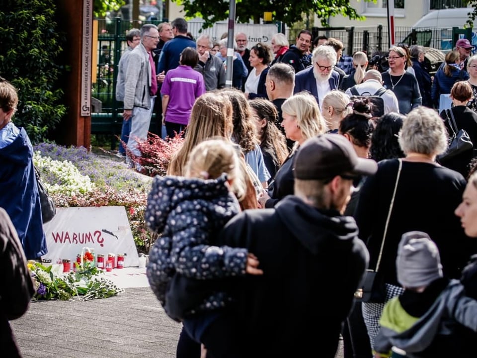 Menschenmenge versammelt sich bei einem Mahnmal mit Blumen und Kerzen.