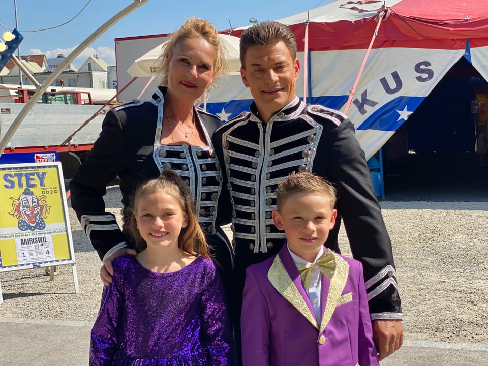 Familie Stey posiert vor dem Zirkuszelt in ihren Kostümen. Die Eltern tragen schwarzes-weiss die Kinder violett.