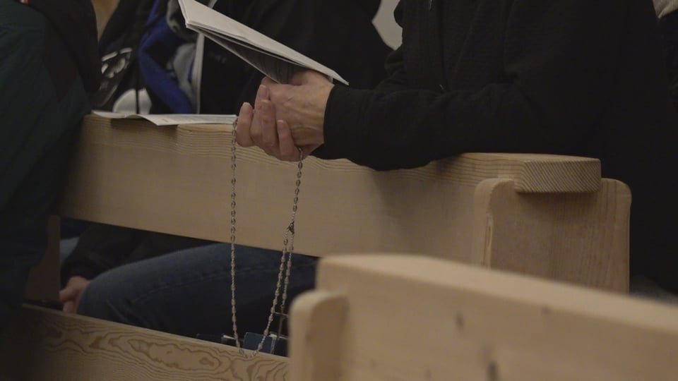 Person mit Rosenkranz in der Hand auf Kirchenbank.