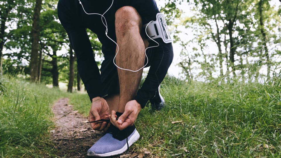 Ein Jogger mit Kopfhörer bindet sich die Schuhe.