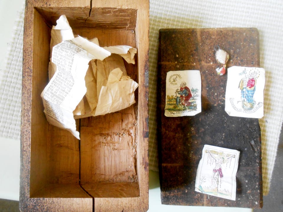 Ein geöffnetes Holzschächtelchen zeigt kleine religiöse Bilder und einen beschrifteten Papierstreifen.