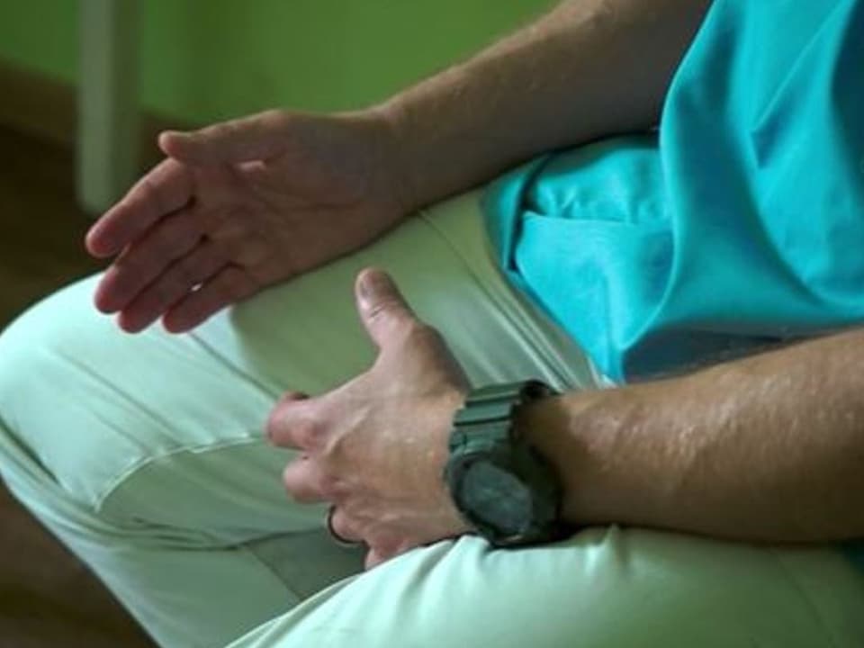 Person in grüner Kleidung mit ausgestreckter Hand und Armbanduhr.