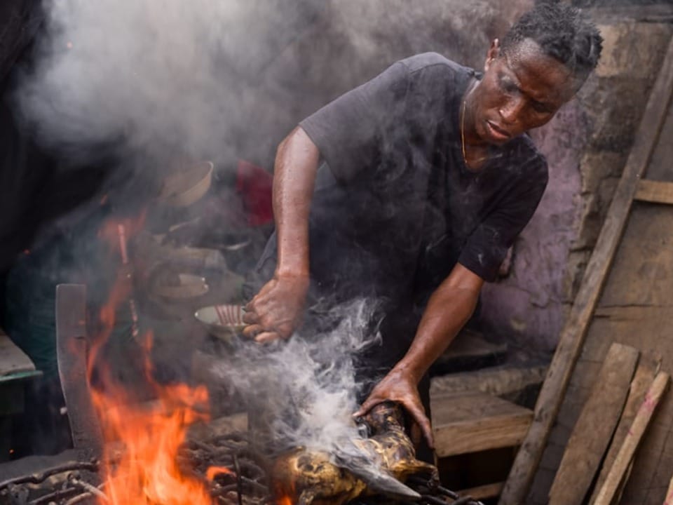 Mann grillt Fleisch über offener Flamme mit viel Rauch.