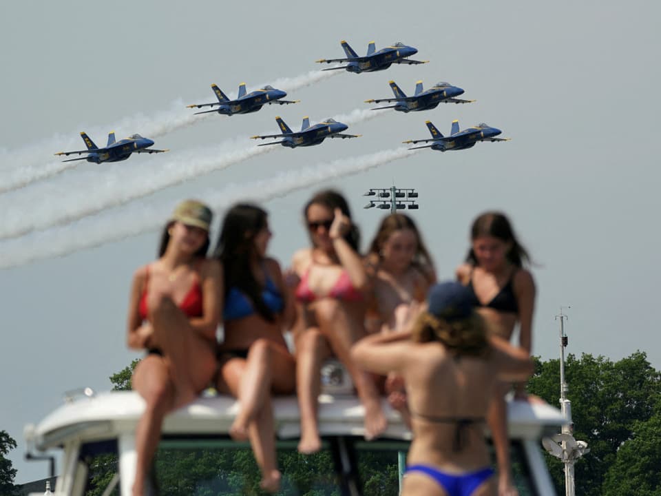 Women in swimsuits on a boat watching six military aircraft