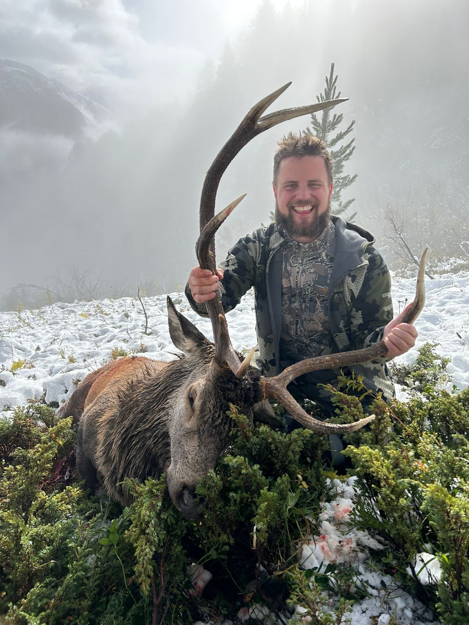 Mann posiert mit erlegtem Hirsch in schneebedeckter Landschaft.