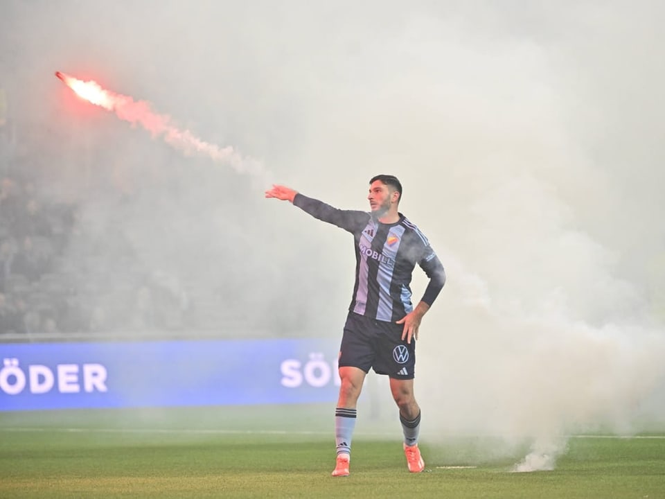 Fussballspieler mit Bengalo auf dem Spielfeld.