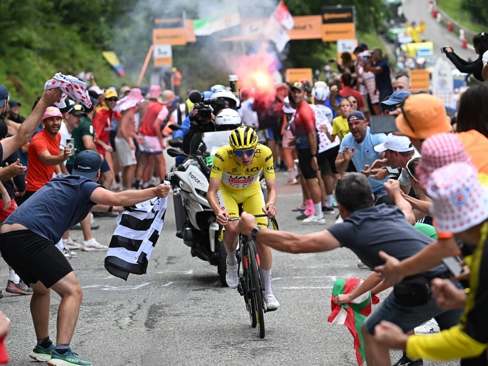 Radrennfahrer in gelbem Trikot von jubelnden Fans auf enger Bergstrasse umgeben.