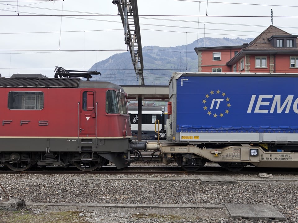 Ein Güterzug, mit einem Lastwagenanhänger beladen, fährt durch einen Bahnhof.