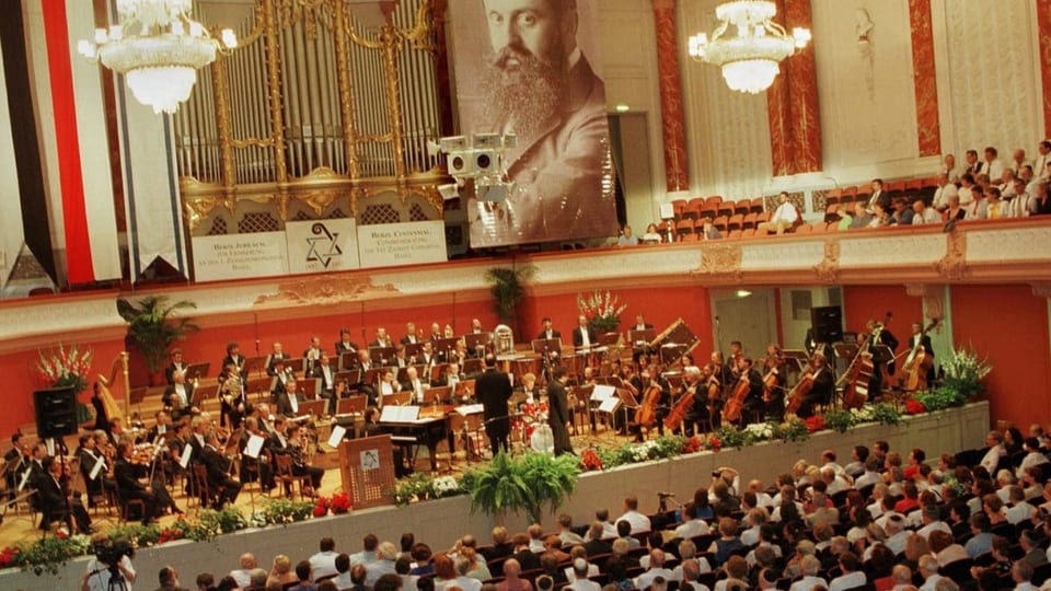 In einem grossen Saal spielt vor Publikum ein klassisches Orchester.