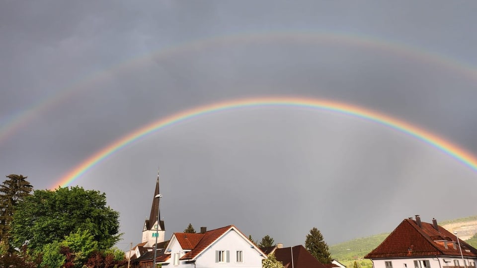 Doppelter Regenbogen über Häuserdächern und Kirche.