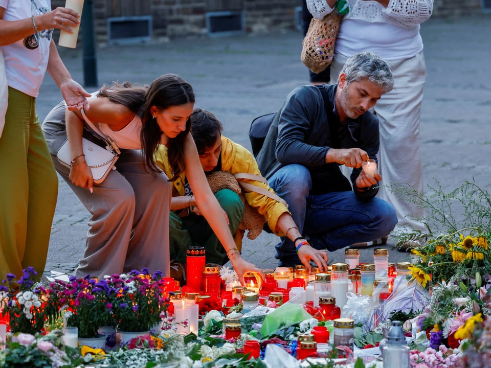 Menschen zünden Kerzen und legen Blumen nieder.