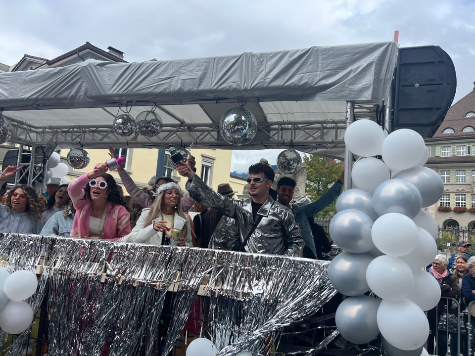 Menschen in Kostümen auf einem geschmückten Festwagen mit Luftballons.