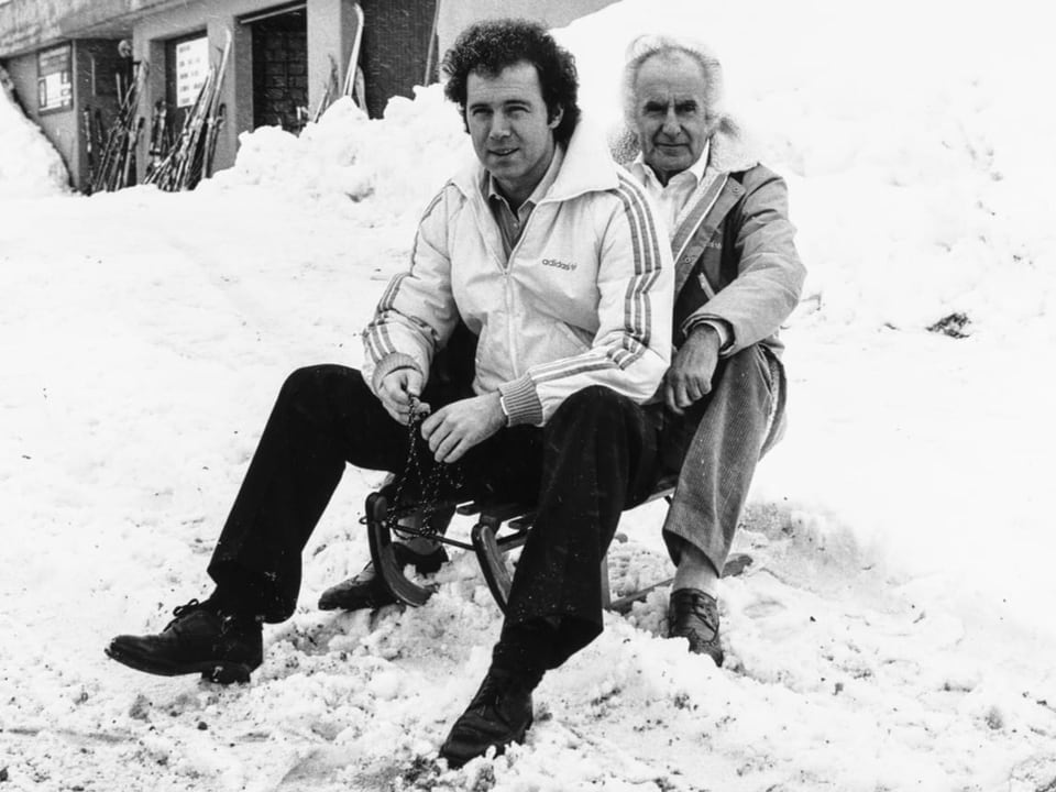 Franz Beckenbauer zusammen mit Robert Schwan auf einem Holzschlitten im Schnee in Sarnen.