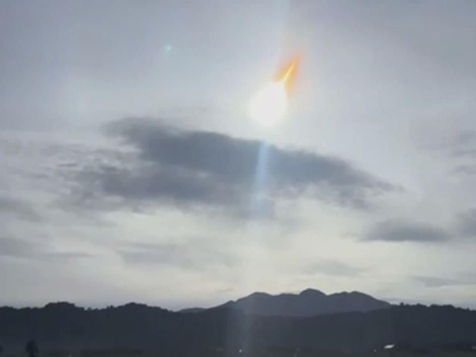 Meteor am Taghimmel über Bergen und Wolken.