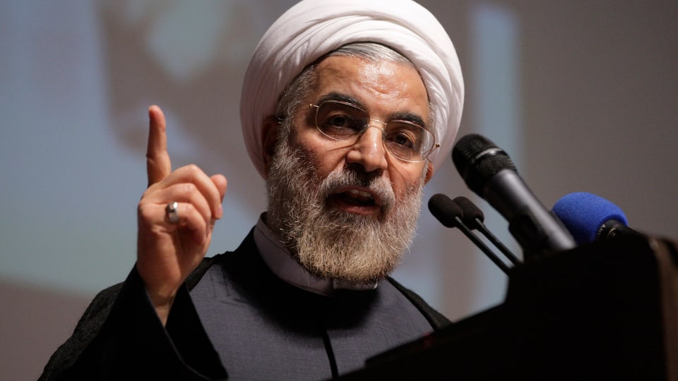 Rohani spricht mit weissem Turban und erhobenem Finger in ein Mikrofon.