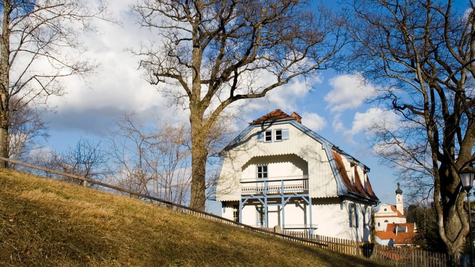 Weissgefärbtes Haus mit winterlichen Bäumen und Kirche im Hintergrund