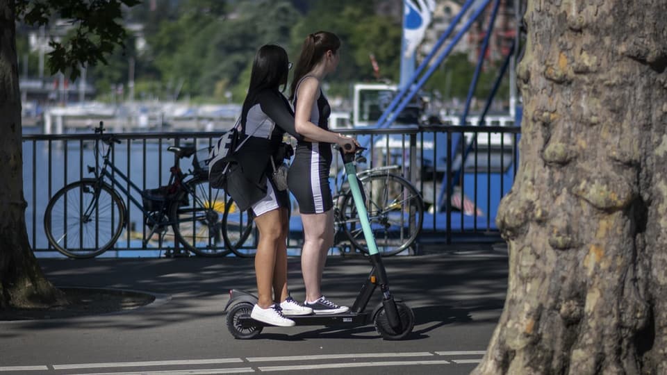 Zwei junge Frauen auf einem E-Scooter, im Hintergrund Brückengelände rund Seebecken