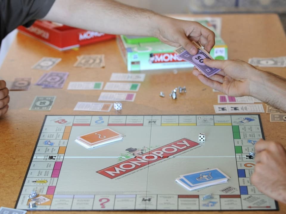 Personen spielen Monopoly und tauschen Spielgeld.