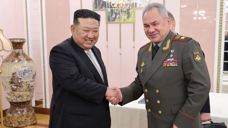 Kim Jong-Und und Sergej Schoigu schütteln die Hände und lächeln in die Kamera