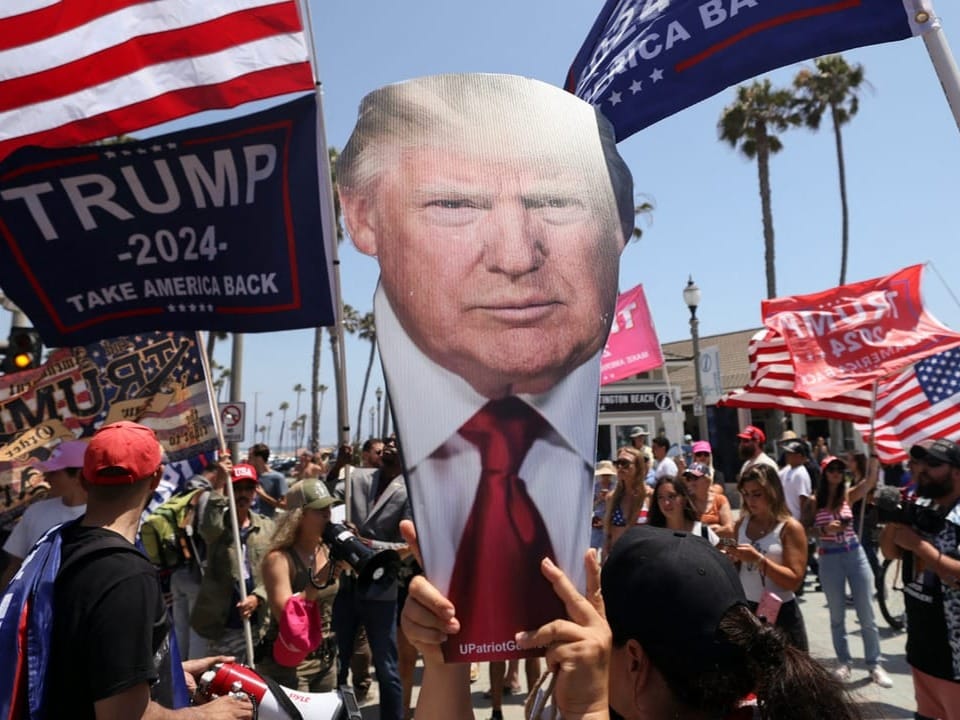 Menschenmenge hält Trump-Schilder und amerikanische Flaggen bei politischer Kundgebung im Freien.
