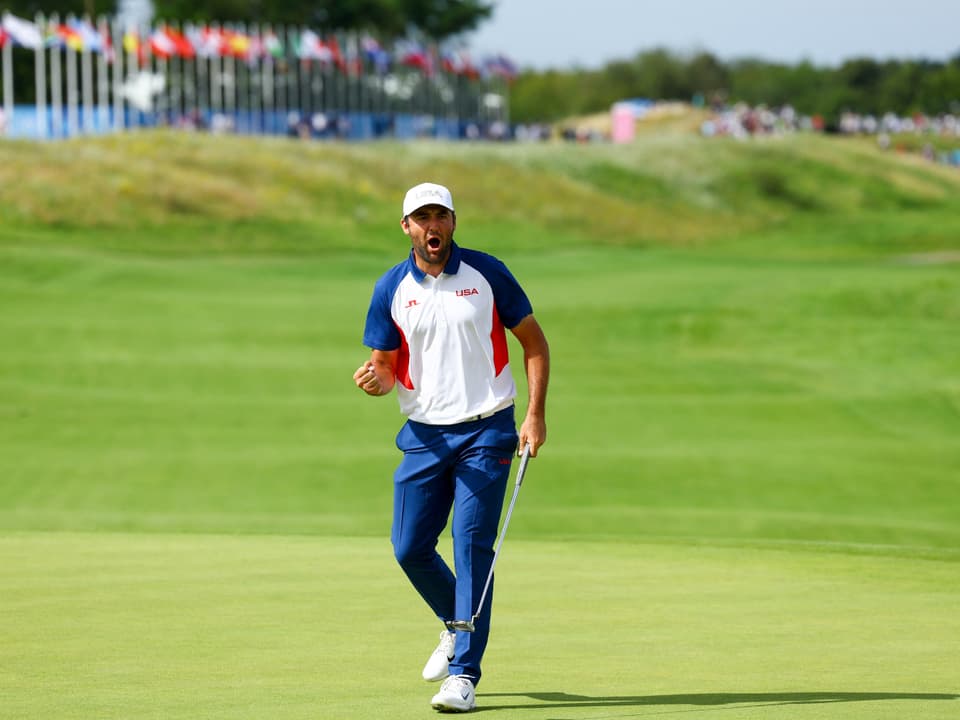 Golfer feiert auf Grün mit Flaggen im Hintergrund.