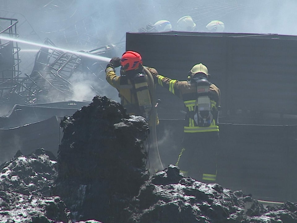 Zwei Feuerwehrleute löschen einen Brand mit einem Schlauch.