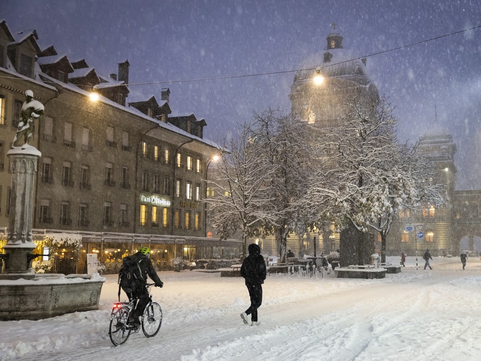 Schneebedeckter Platz mit Radfahrern und Fussgängern.