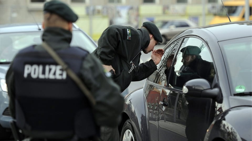 Zwei Polizisten vor einem Auto: Der eine schaut in die Rückscheibe des Fahrzeugs, der andere überwacht.