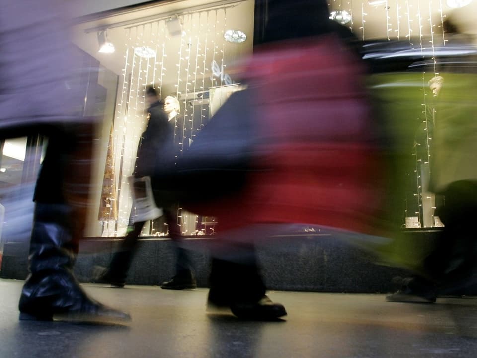 Man sieht Leute mit Taschen in der Bewegungsunschärfe und ein weihnächtliches Schaufenster.