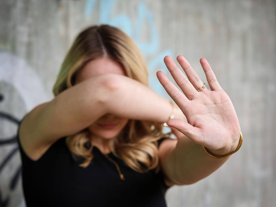 Frau verdeckt Gesicht mit Arm und Hand.