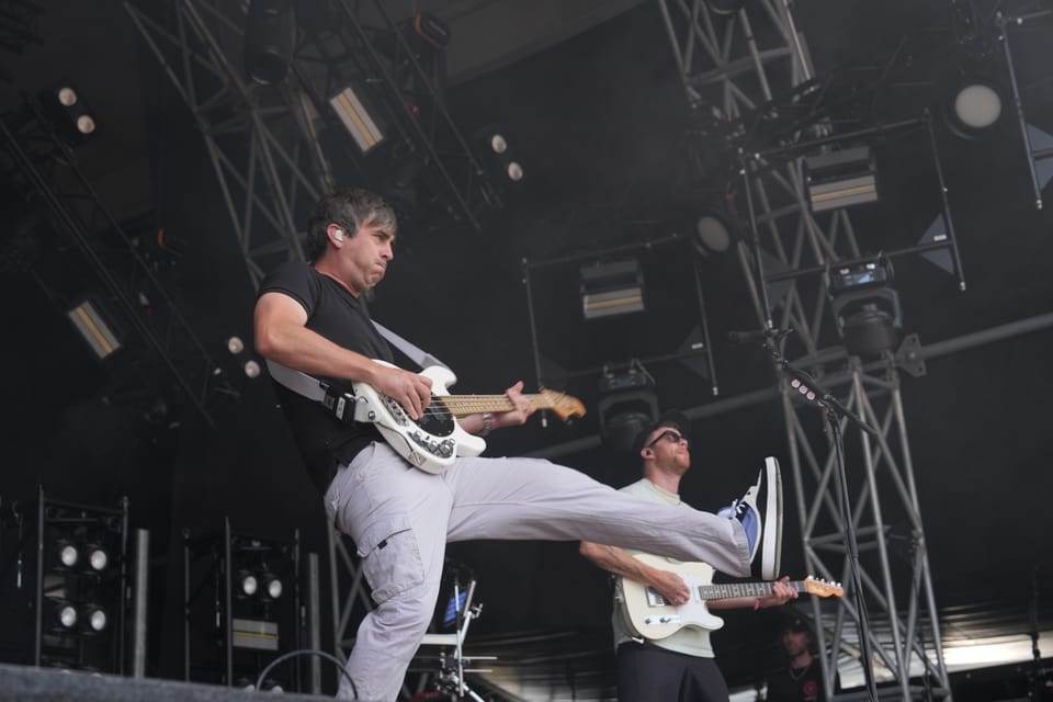 Gitarrist auf der Bühne hebt Bein, weiterer Musiker im Hintergrund am Open Air Lumnezia 2024.