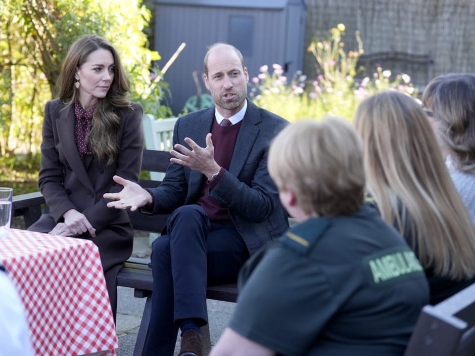 Kate und William sitzen mit anderen Leuten um einen Tisch und sprechen mit ihnen.