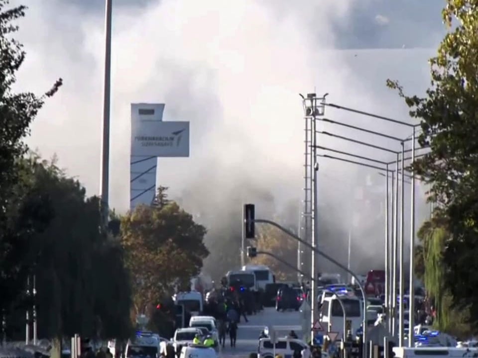 Strasse mit Rauchwolken im Hintergrund, plus Fahrzeuge und Menschen.