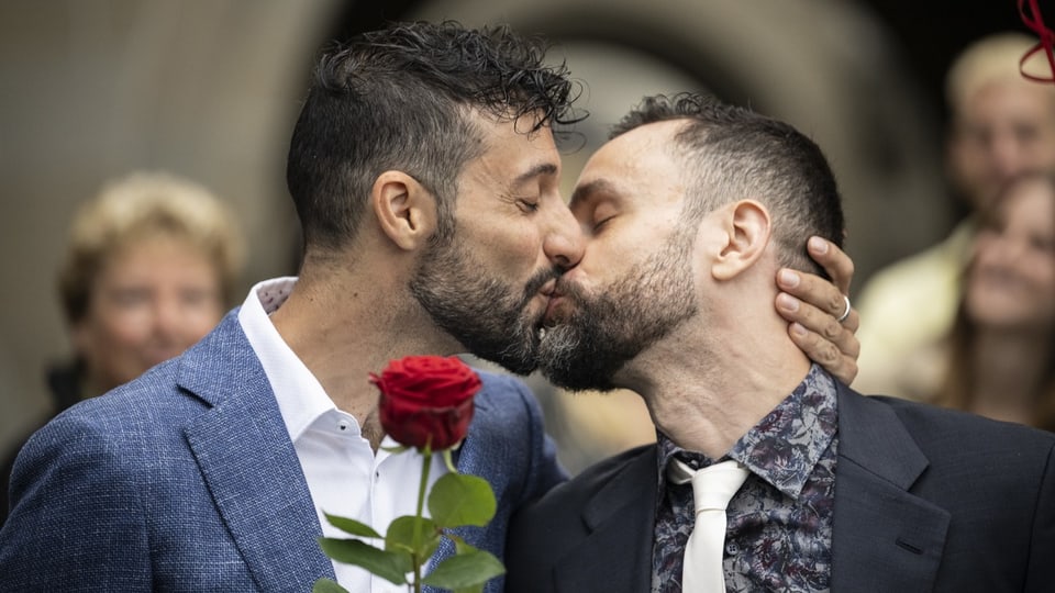 Zwei Männer küssen sich nach der Trauung. Der eine hält eine Rose in der Hand.