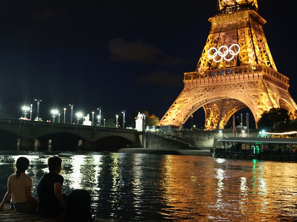 Nachts am Seine-Ufer mit beleuchtetem Eiffelturm und Olympischen Ringen.