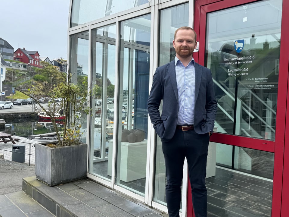 Mann in Anzug vor einem Gebäude mit rotem Rahmen und Glastür stehend.