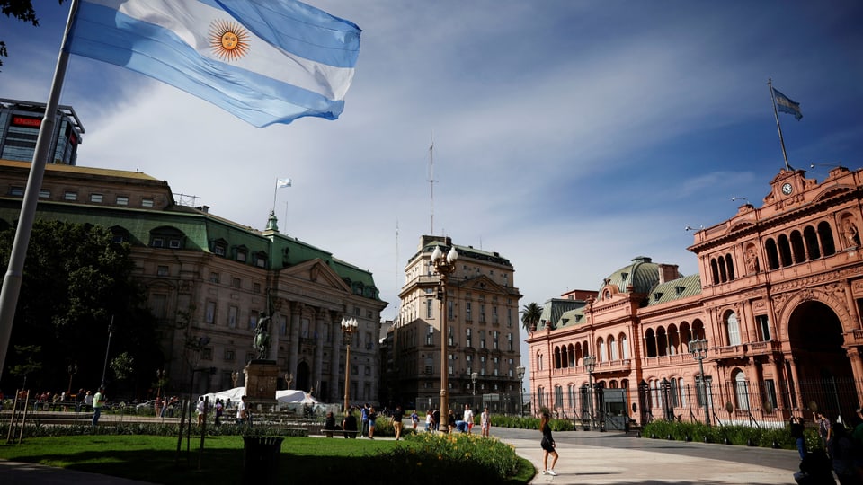 Argentinische Flagge weht vor historischen Gebäuden bei sonnigem Himmel.