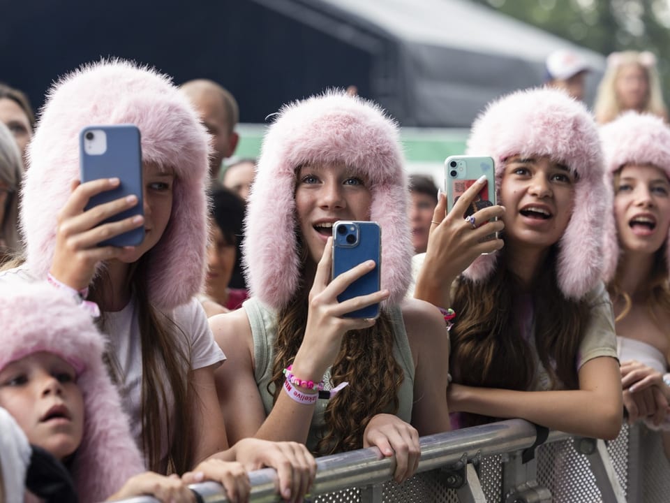 Gruppe von Mädchen mit rosa Fellmützen beim Fotografieren auf einem Konzert.