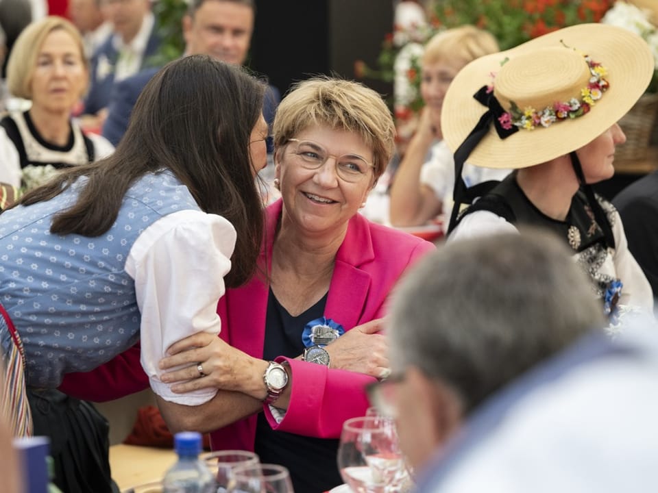 Frau in rosa Blazer lächelt, während eine andere Frau sie umarmt.