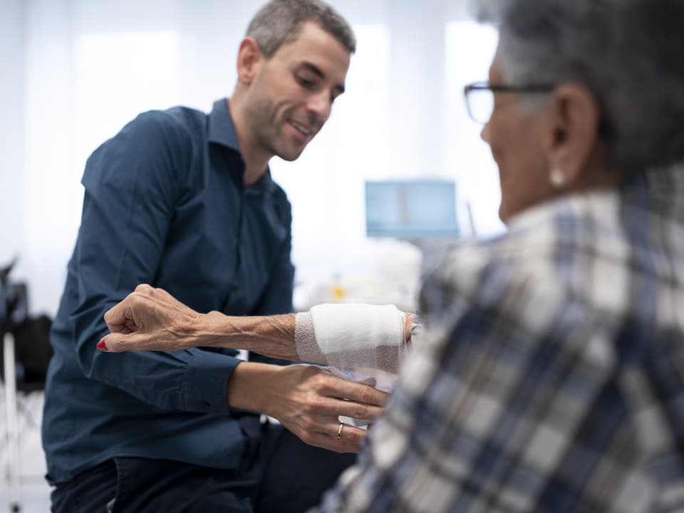 Ein Hausarzt macht einer Patientin einen Verband.