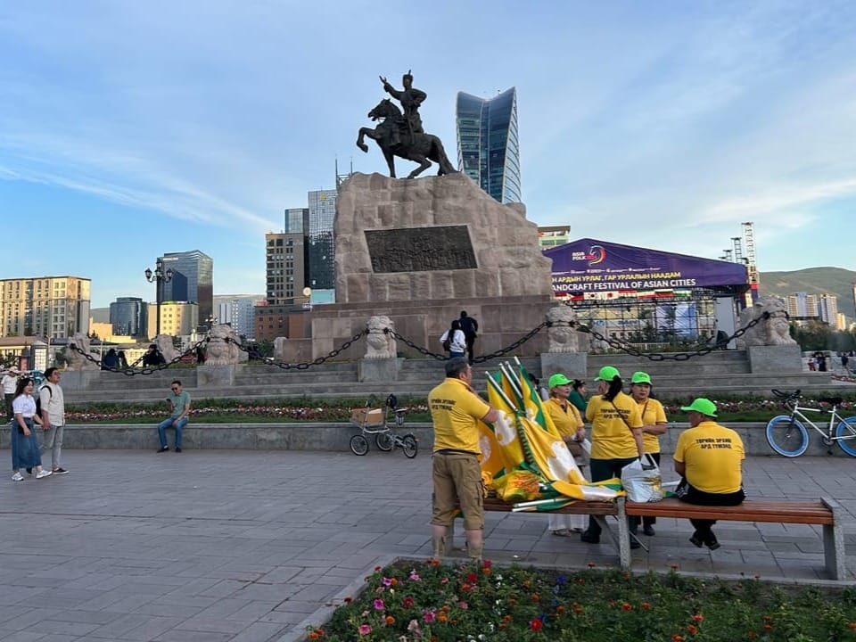 Personen in gelben T-Shirts vor einer Reiterstatue auf einem Platz in der Stadt.