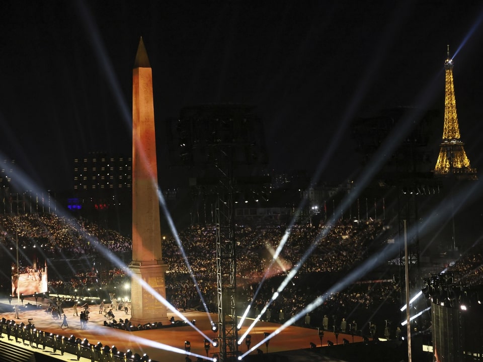 Beleuchtetes Fest mit Obelisk und Eiffelturm bei Nacht.