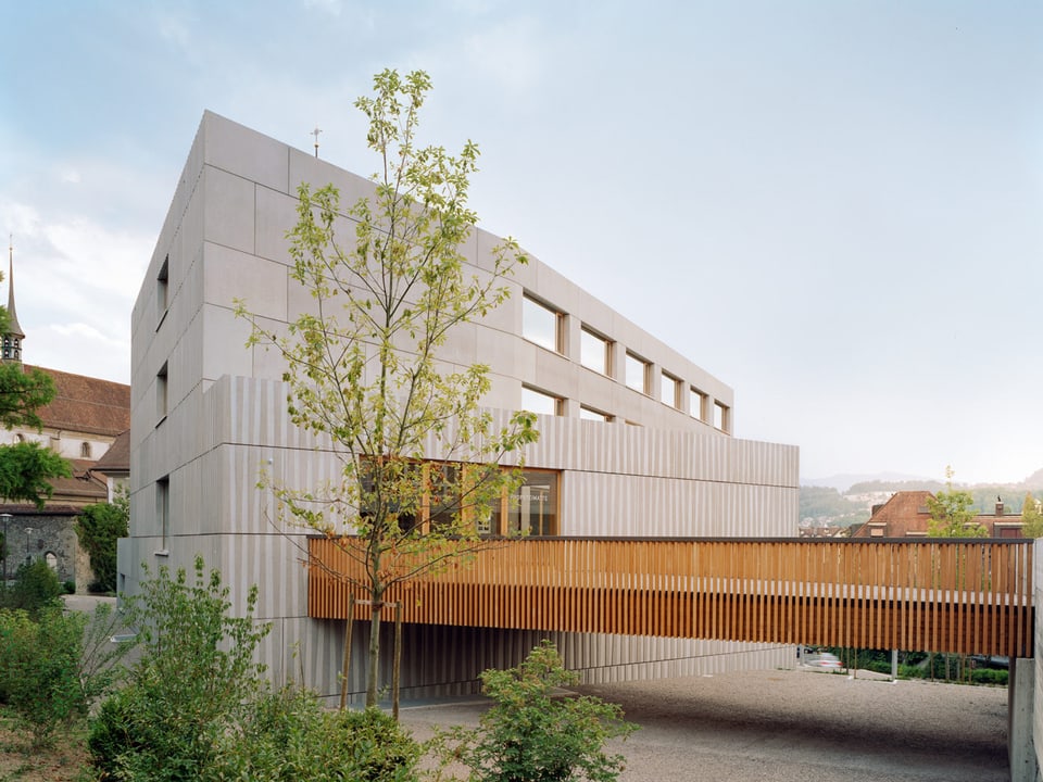 Modernes Gebäude (Schulhaus) mit einem überdachten Verbindungsgang aus Holz. 