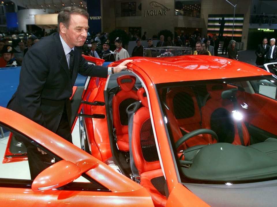 Mann präsentiert rotes Auto auf Automesse.